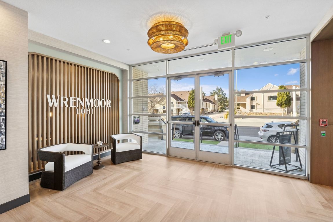 Entrance lobby with glass doors, seating, and gold light fixture; wooden accents and exterior view.