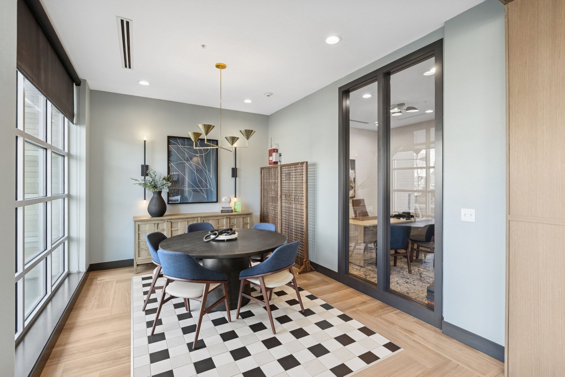 Modern dining room with a black table, blue chairs, large windows, and a checkered rug