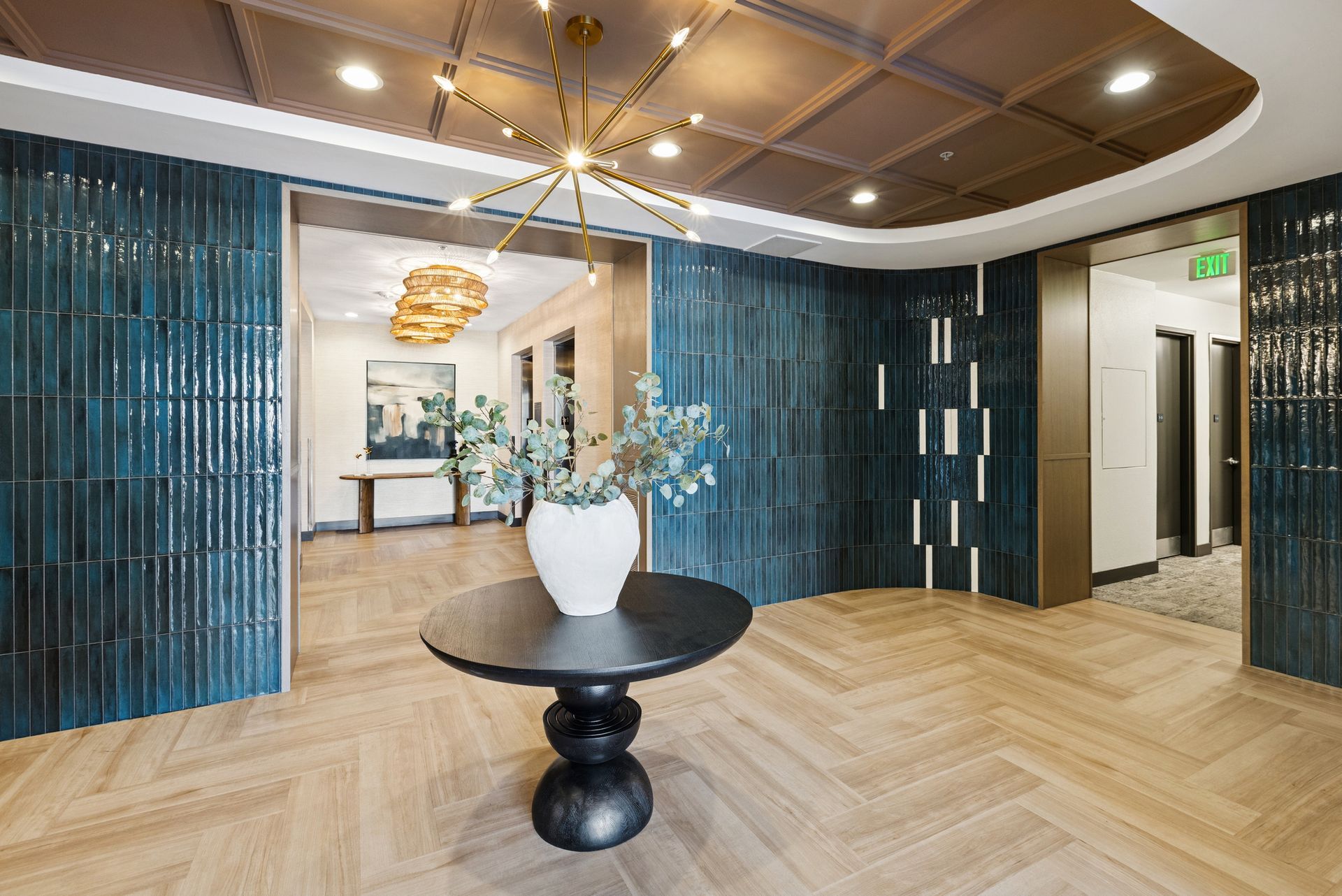 Modern lobby with blue tiled walls, wood ceiling, and a small round table with a white vase.