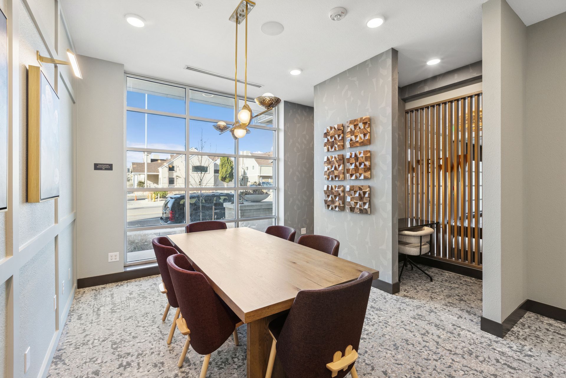 Modern dining room with a wooden table, dark chairs, and large windows overlooking a street.