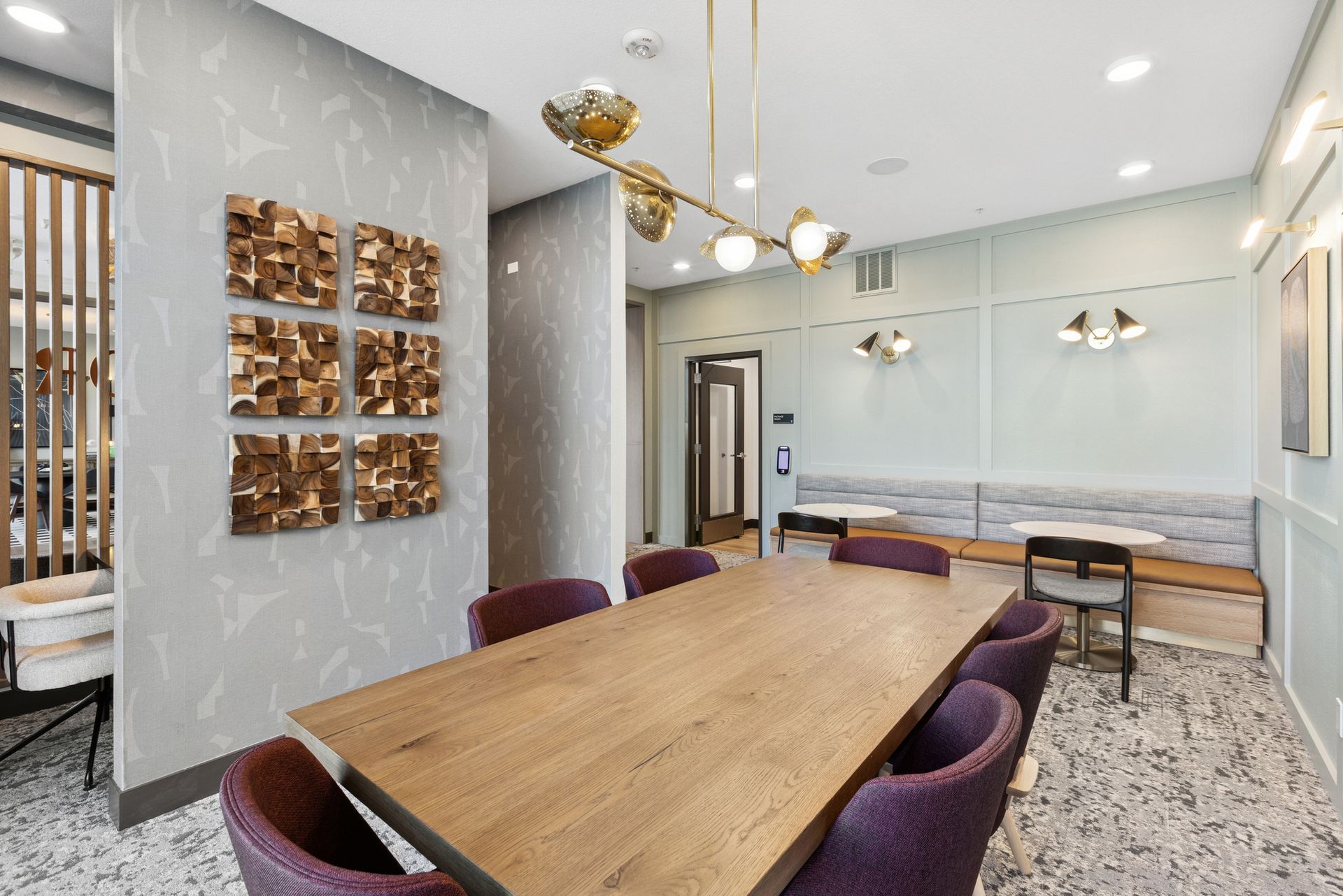 Modern meeting room with wooden table, purple chairs, marble walls, and gold-accent pendant lights
