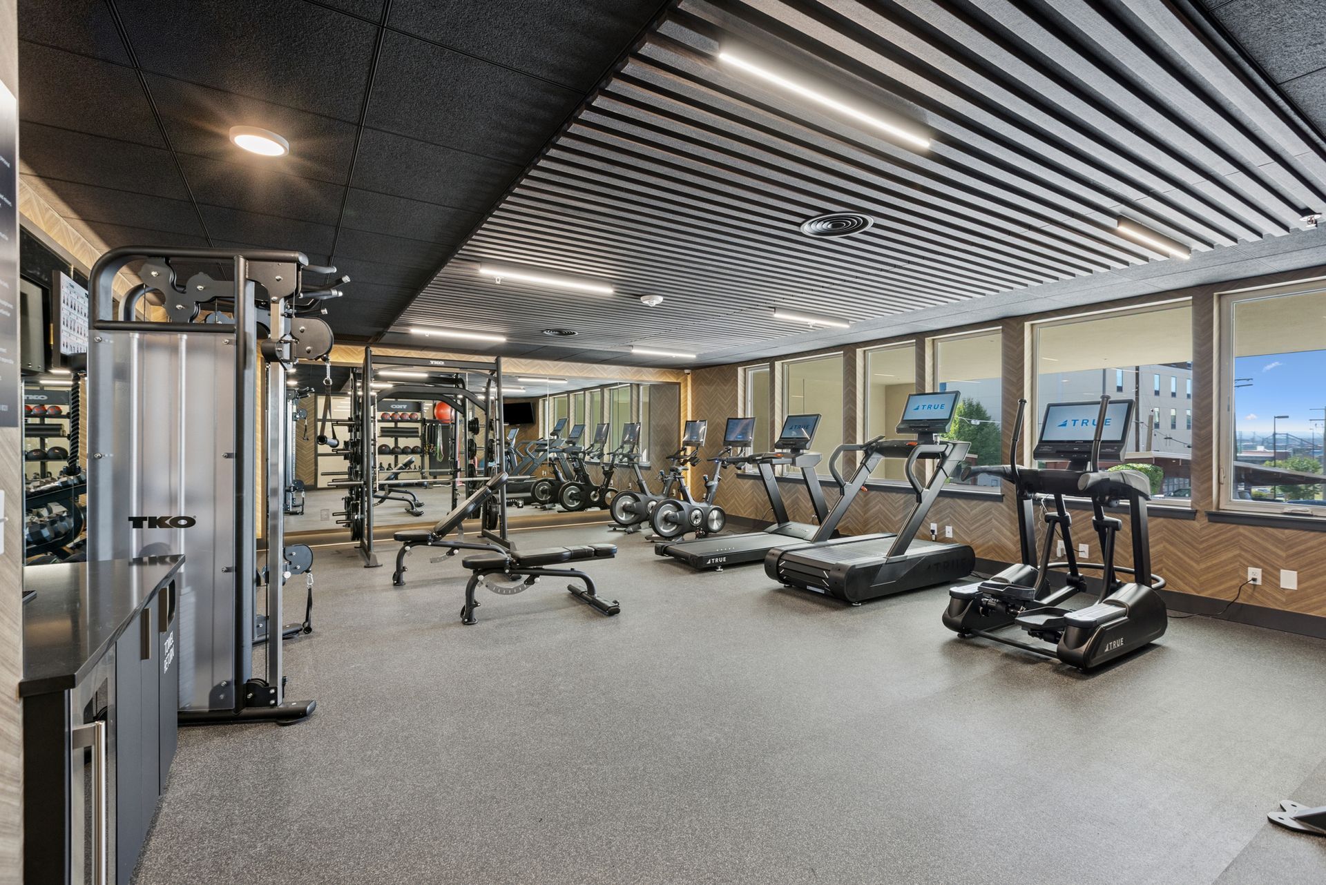 Modern gym interior with treadmills, weights, and exercise machines under striped ceiling panels