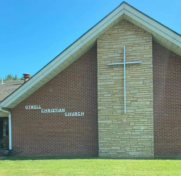 Brick church building with a tan stone cross on the front and a green lawn under a blue sky