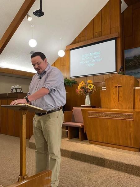 Man standing at a church lectern with a projected slide and wooden pulpit in the background