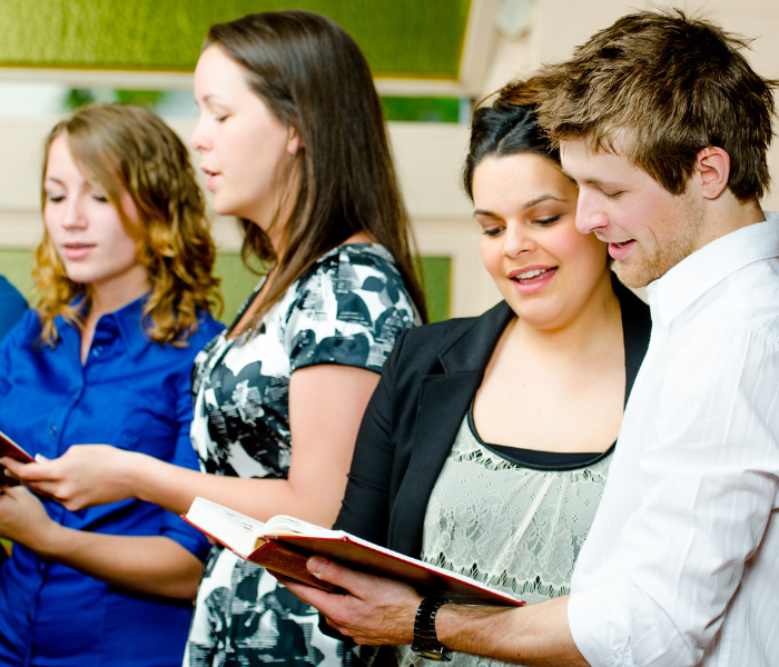 Four people standing together, smiling and reading from an open book indoors