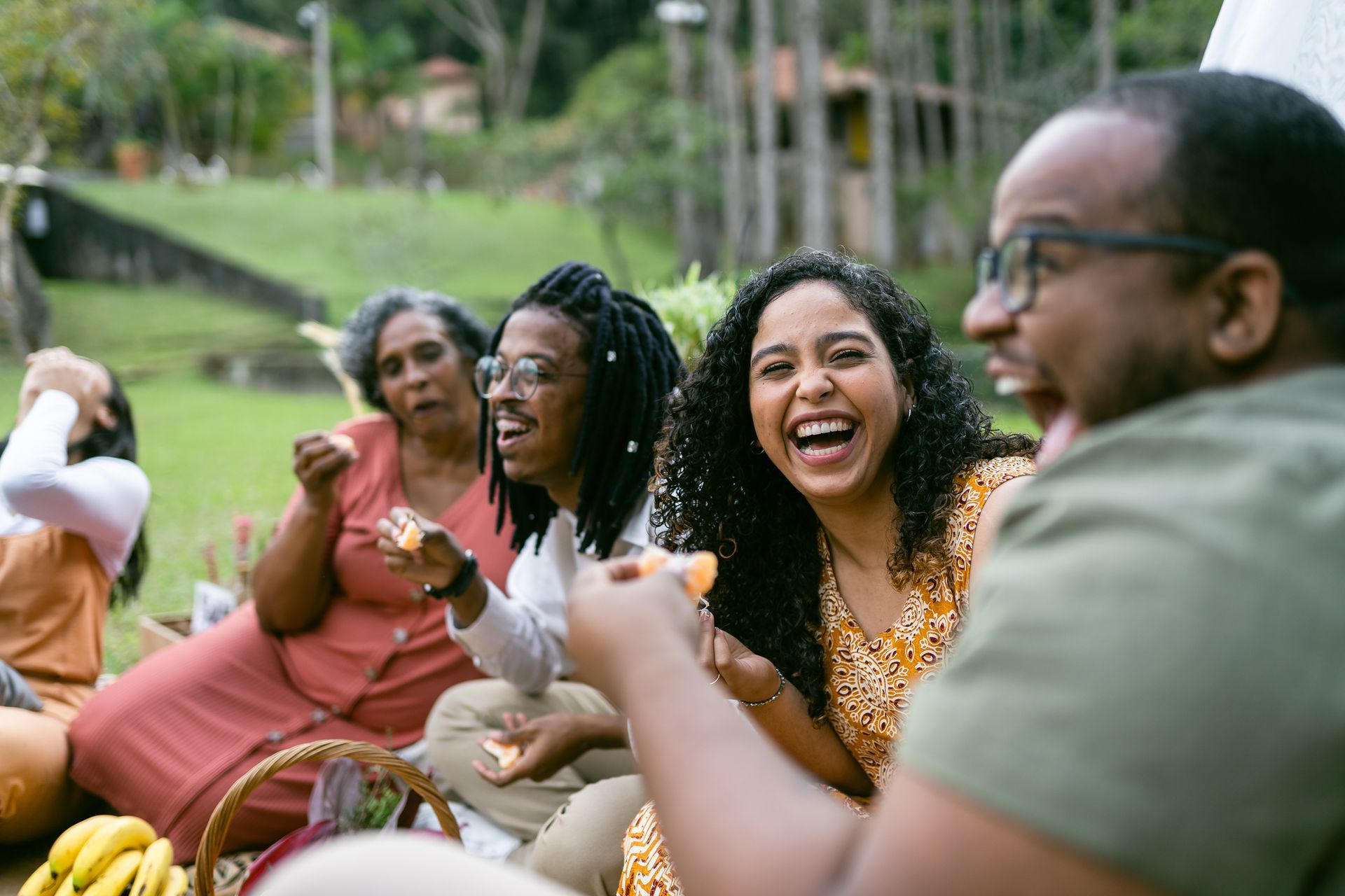 Smiling friends enjoying a picnic together at a scenic holiday park during a sunny afternoon outing Smiling friends enjoying a picnic together at a scenic holiday park during a sunny afternoon outing