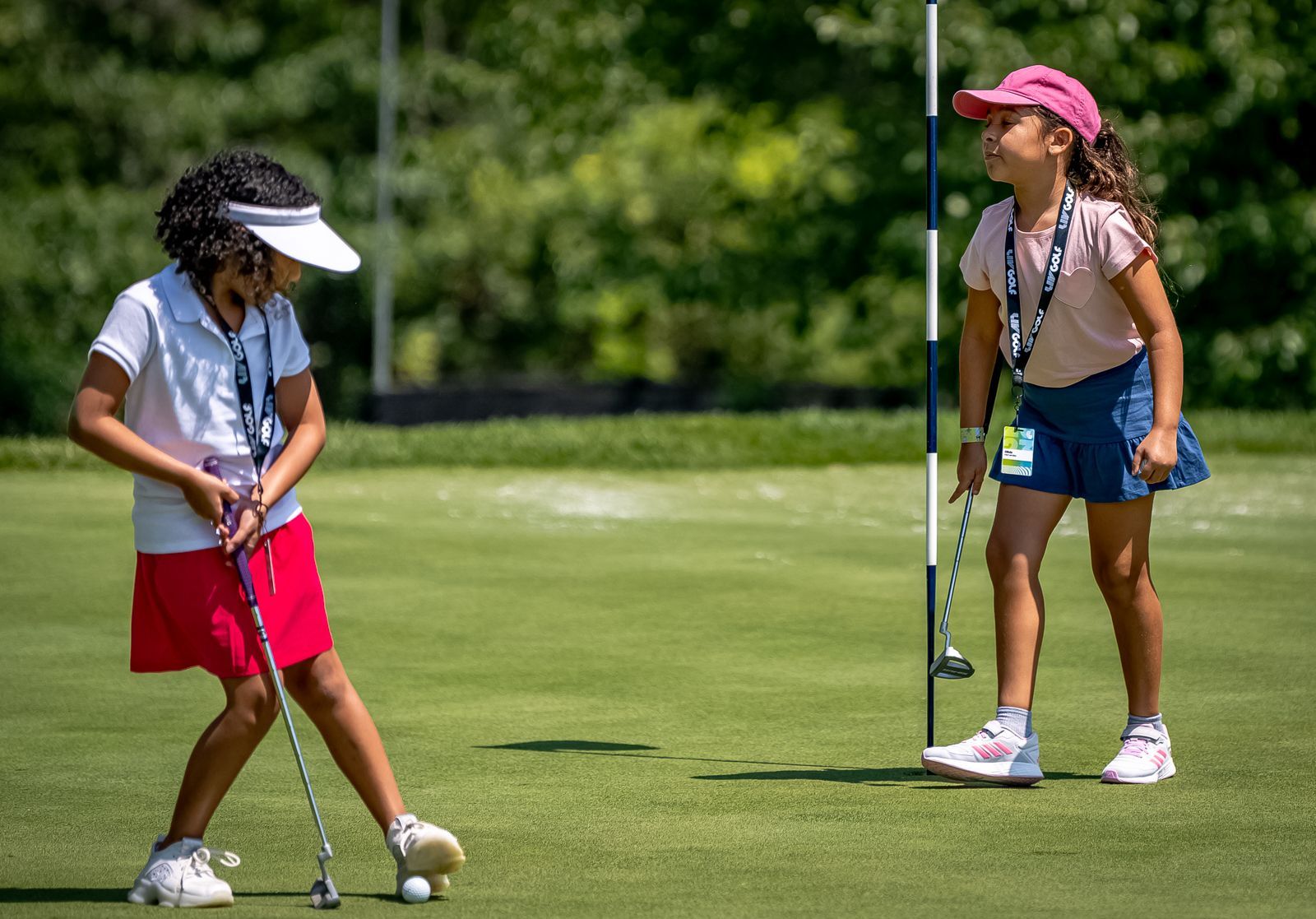 Two girls on a putting green, one putting while the other watches.