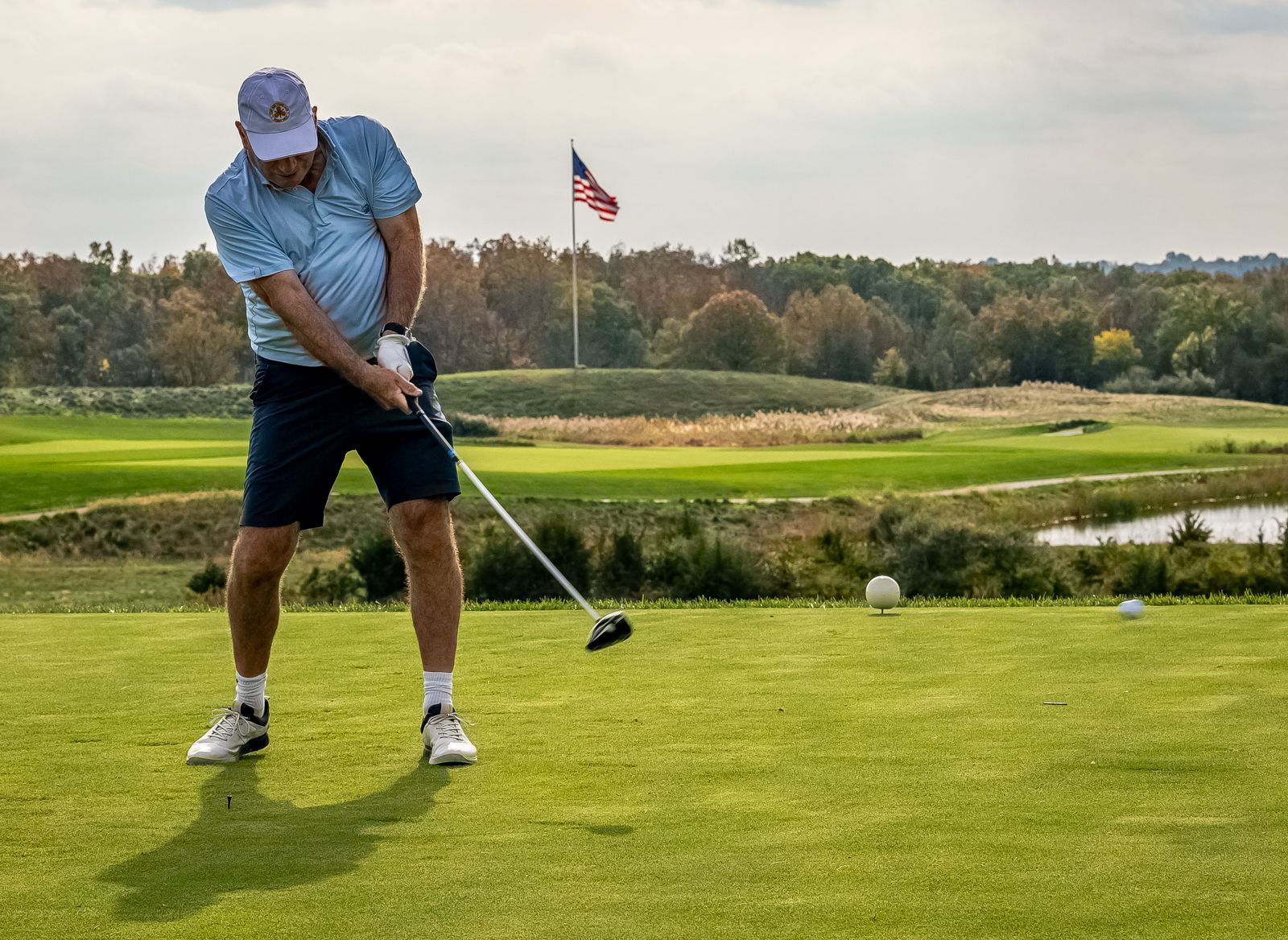 Golfer swinging on a green; golf course with American flag in background.