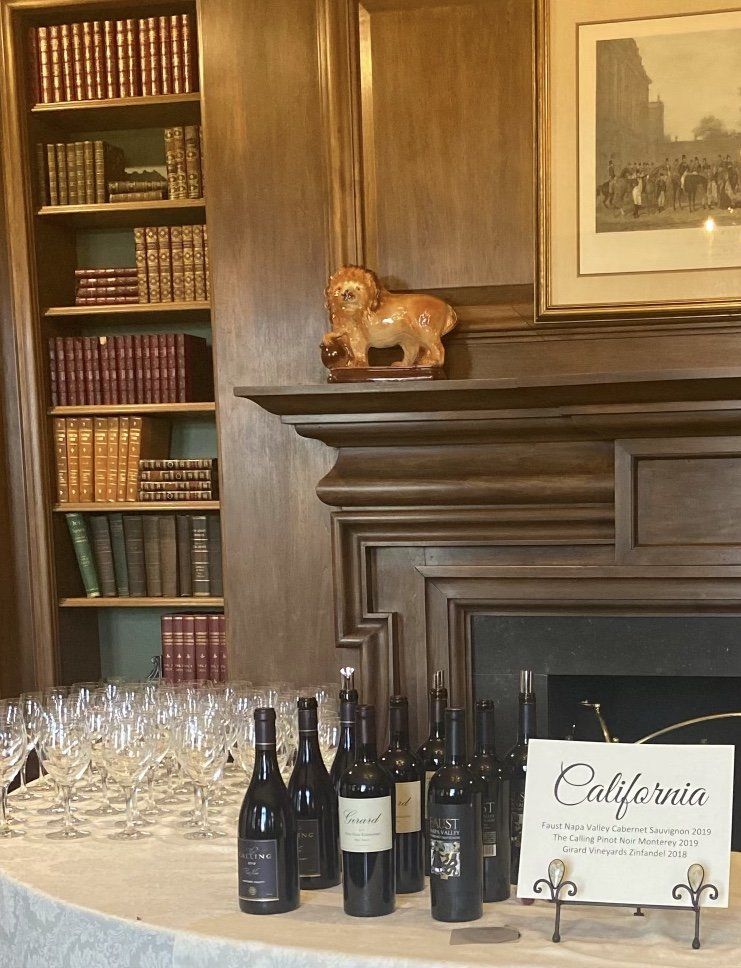 Wine bottles displayed on a table in front of a fireplace with bookshelves.