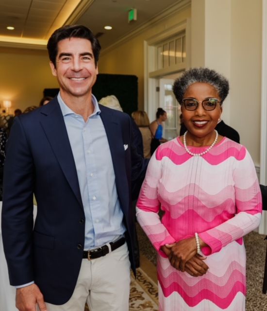 Man in navy blazer and woman in pink patterned dress posing indoors.