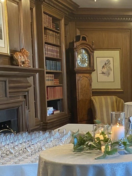 Elegant room with a grandfather clock, bookshelves, fireplace, and tables set for a gathering.