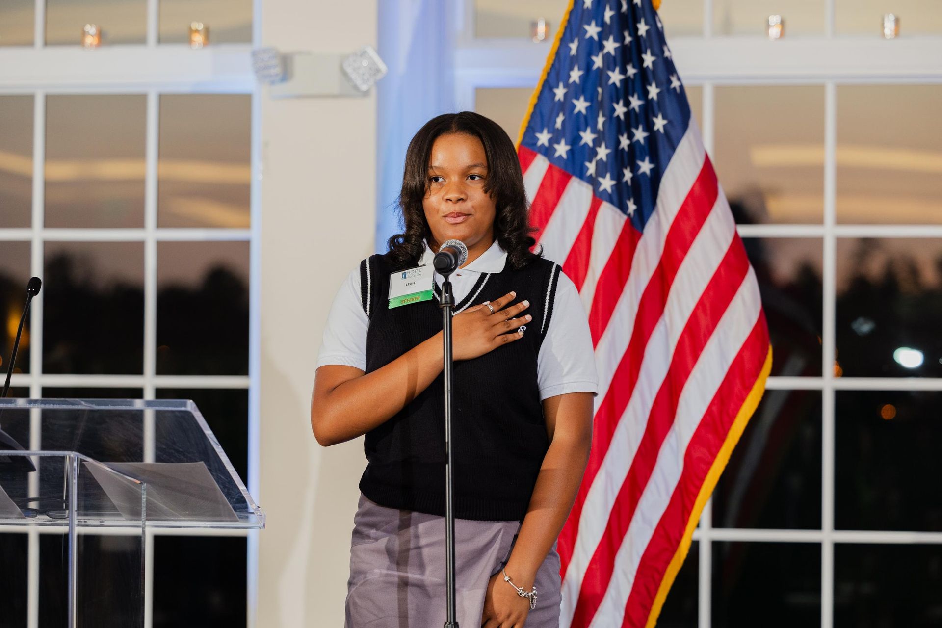 Woman reciting the Pledge of Allegiance with hand over heart, near an American flag.
