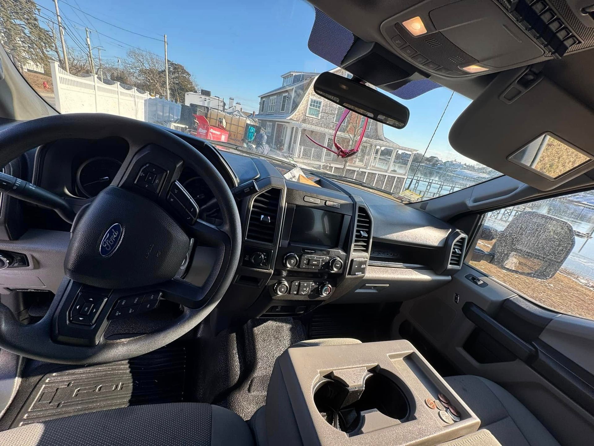 Interior view of a dark-colored Ford truck dashboard, steering wheel, and front center console on a sunny day.