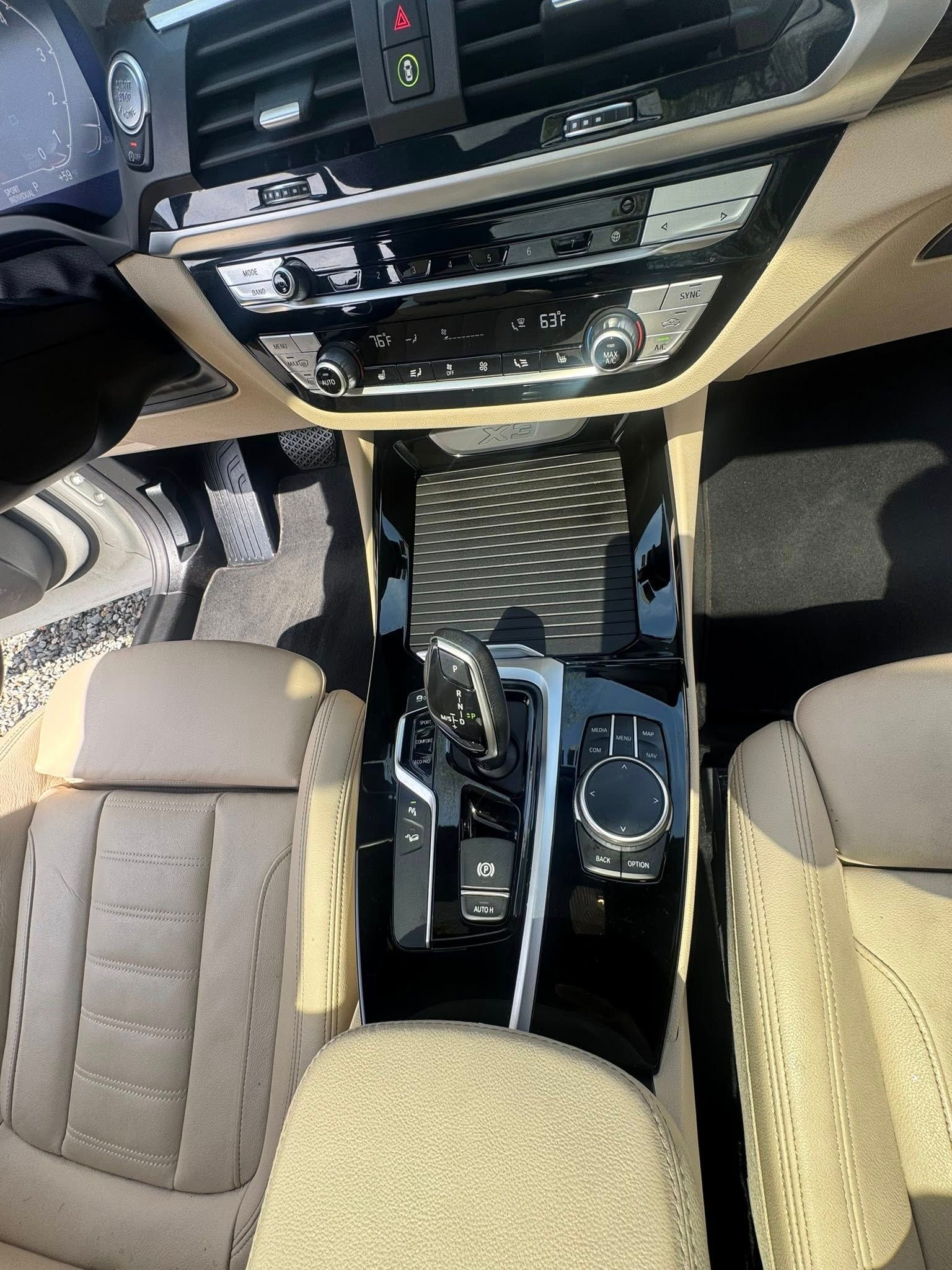 A top-down view of a luxury car's center console featuring tan leather seats, a gear shifter, and dashboard controls.