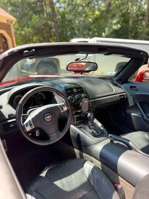 The interior of a red convertible car showing the steering wheel, dashboard, and driver's seat on a sunny day.