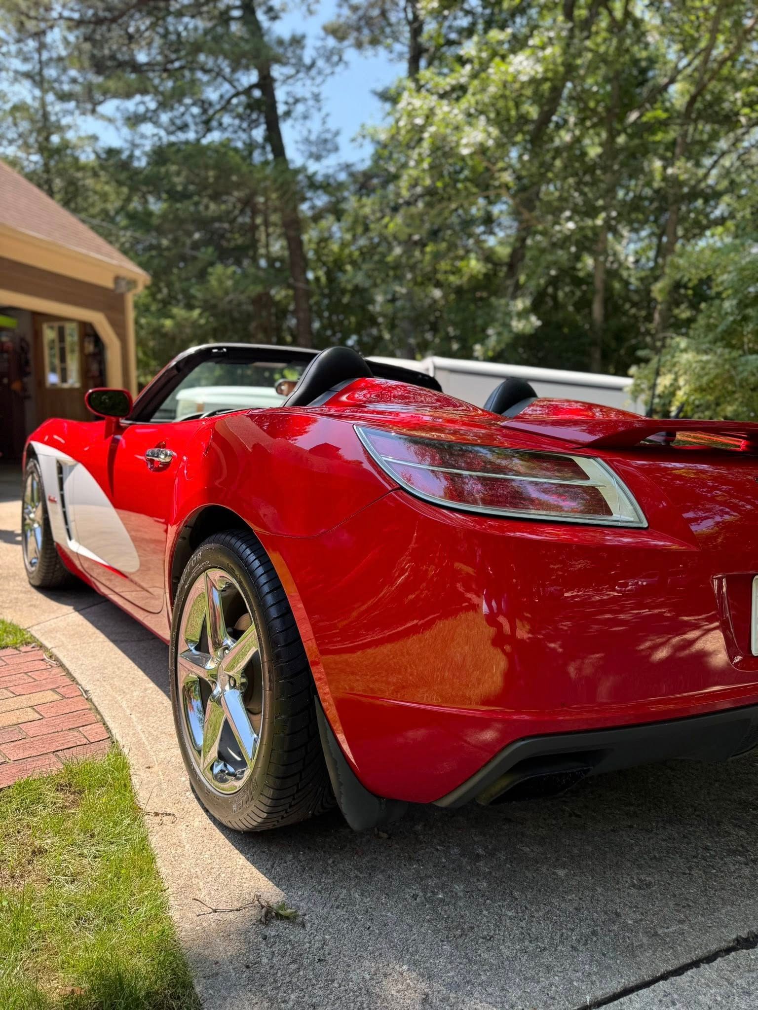 A red convertible sports car parked on a concrete driveway near a house exterior.
