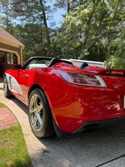 A shiny red convertible sports car with chrome wheels parked in a driveway on a sunny day.