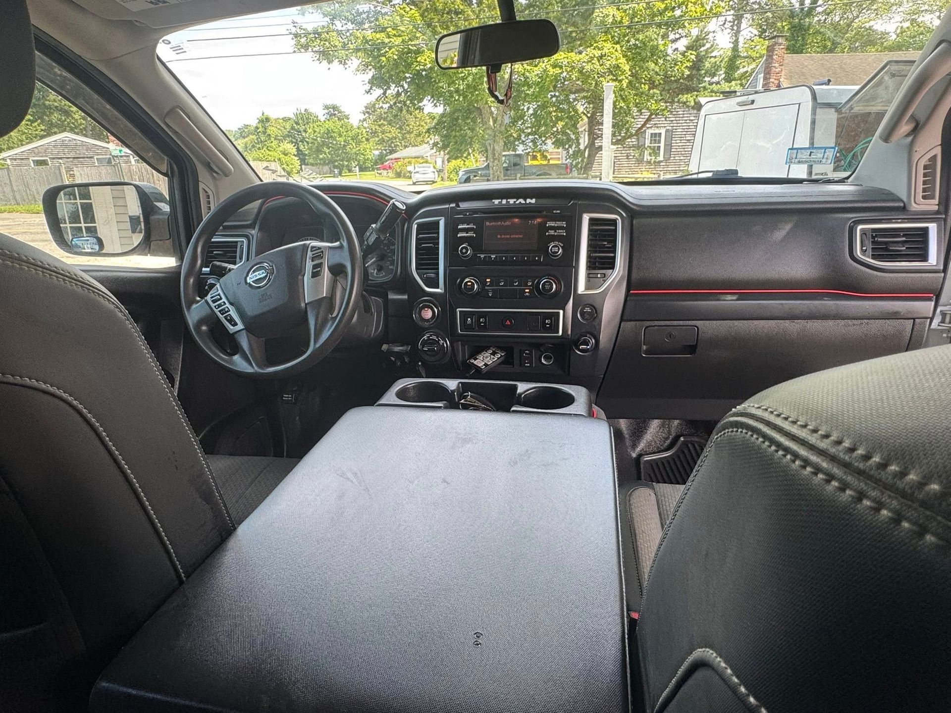 Interior view of a vehicle dashboard, steering wheel, and a large black center console from the back seat.