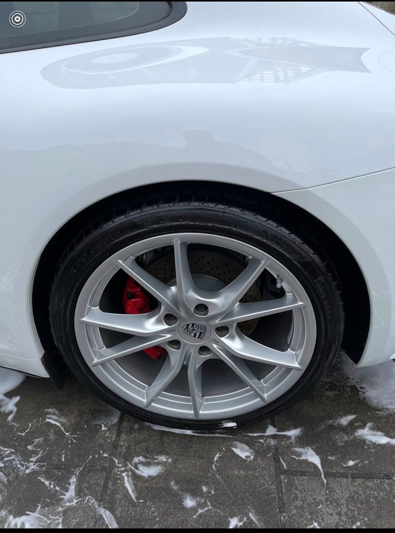 A close-up of a clean white car's silver alloy wheel with a red brake caliper, parked on a wet paved surface.