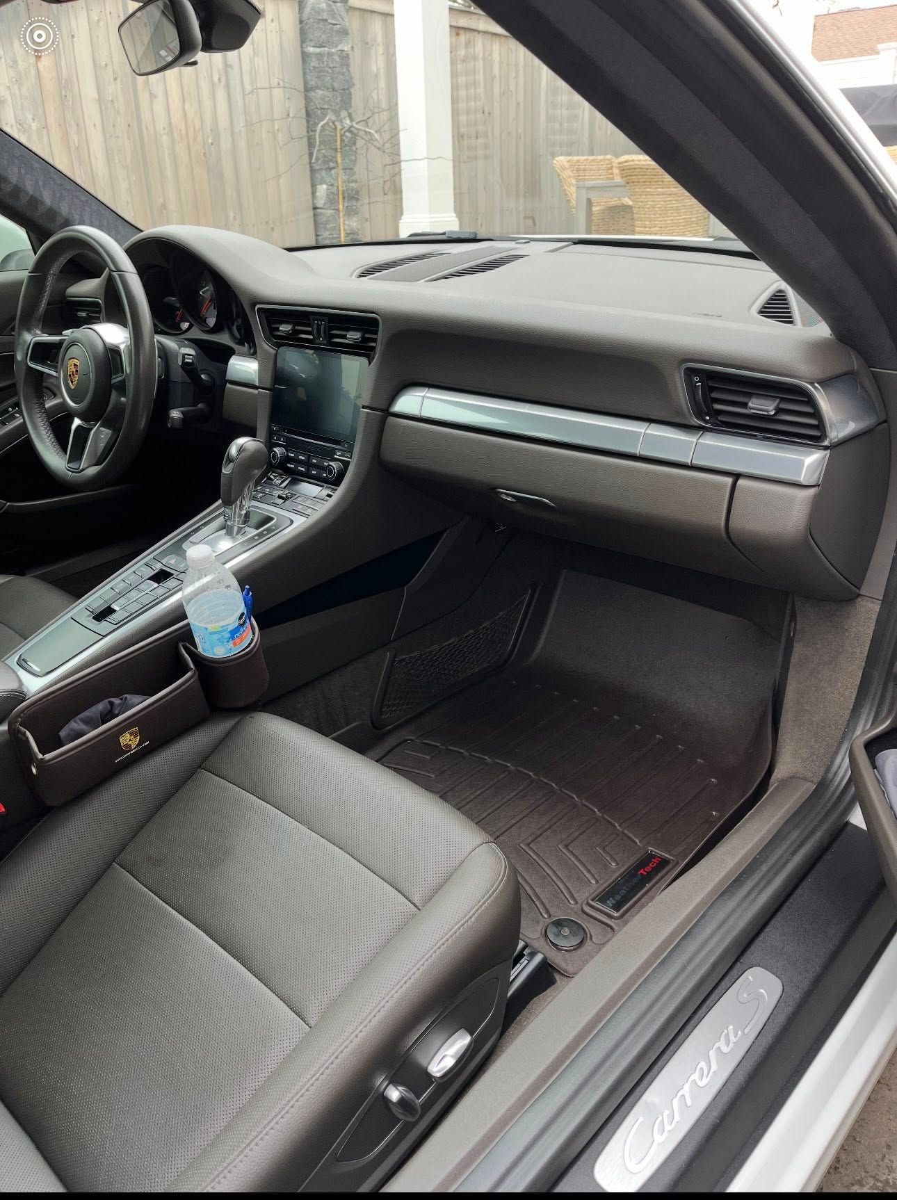 The interior of a Porsche Cayenne showing dark leather seats, a central touchscreen, and custom fitted floor mats.