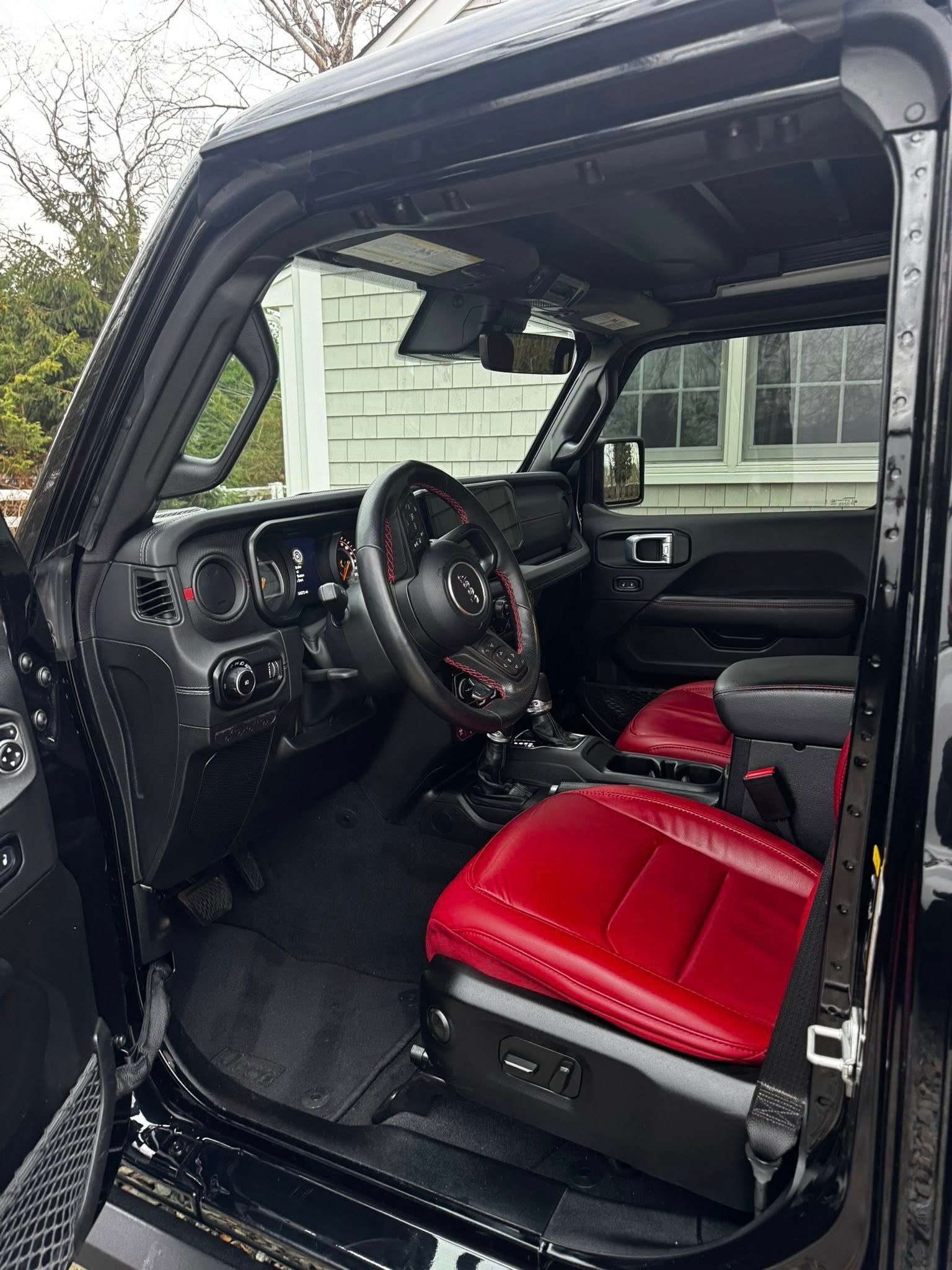 Interior of a black Jeep with red leather seats, viewed from the open driver-side door.