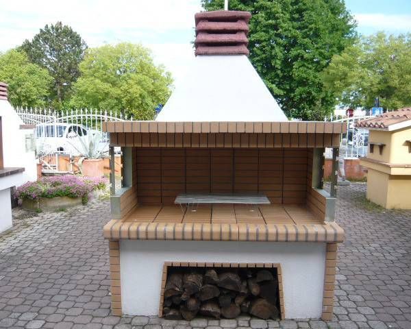 Barbecue esterno in mattoni con vano per la legna, piano di lavoro piastrellato e camino, situato in un cortile.