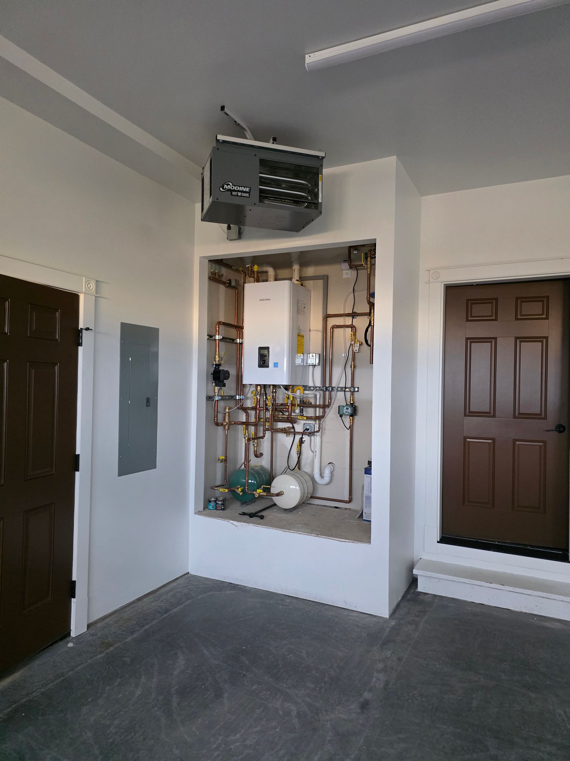 Indoor utility closet with exposed plumbing, valves, and electrical panels in a white hallway.