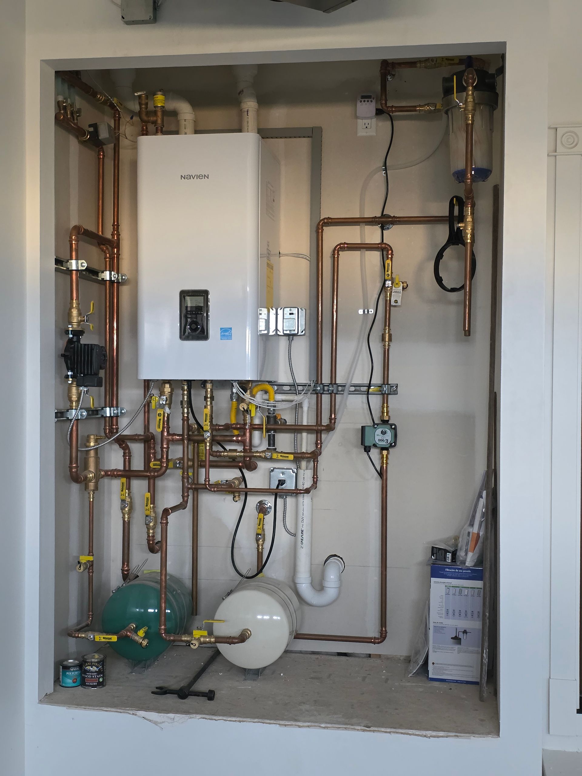 Utility room with wall-mounted boiler, copper pipes, valves, and expansion tanks inside a recessed alcove