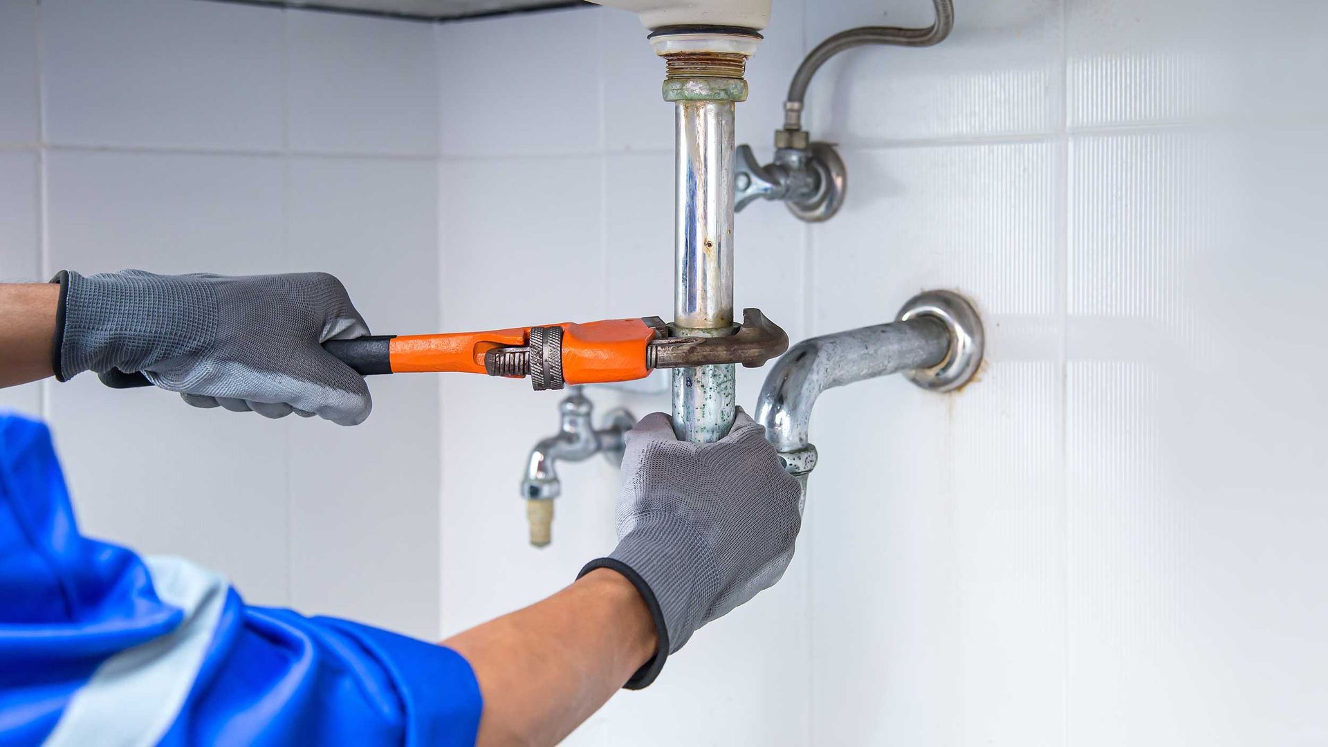 Plumber using a wrench to repair a water pipe under the sink.