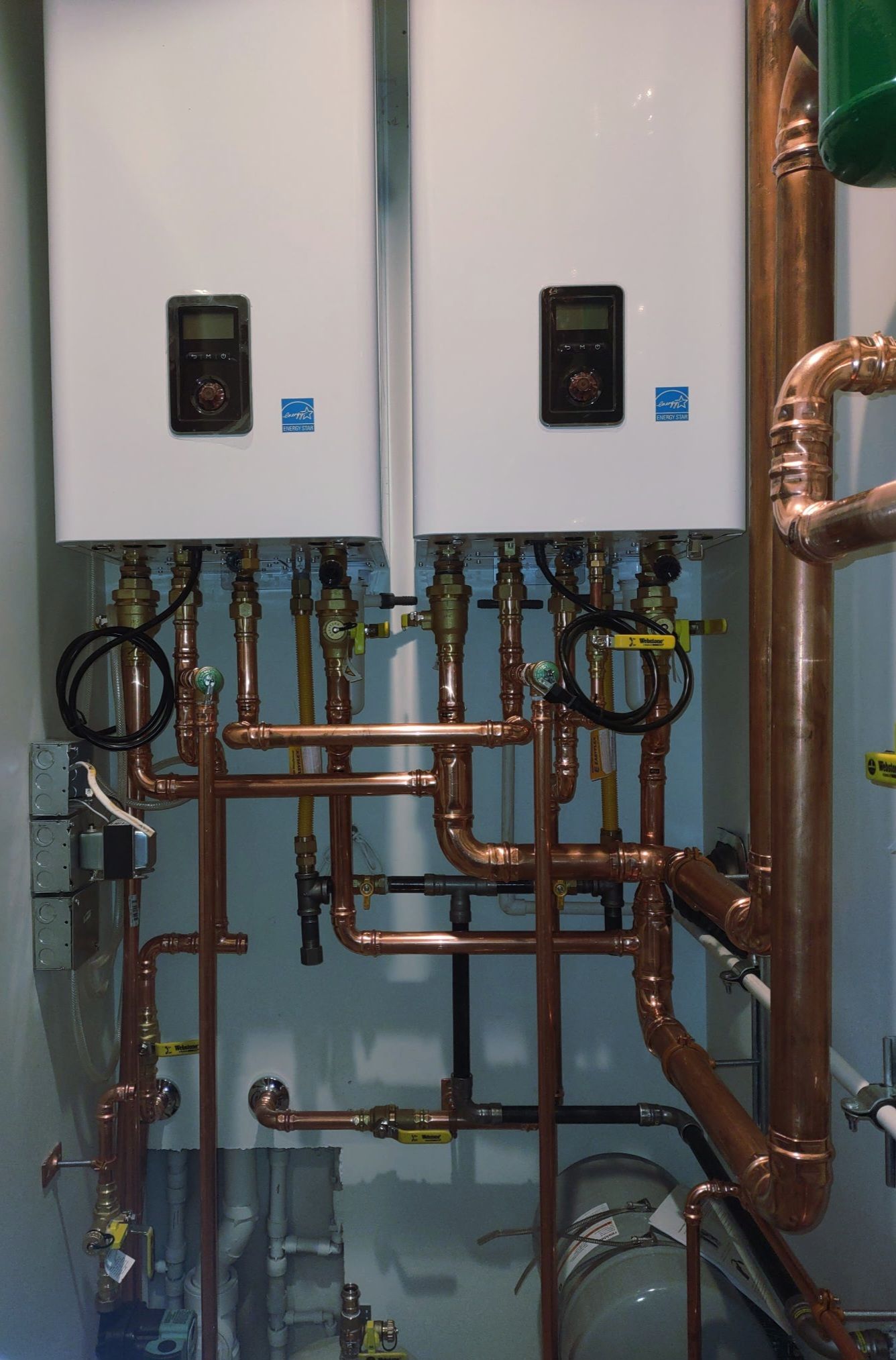 Boiler room with two white water heaters and exposed copper piping on a wall