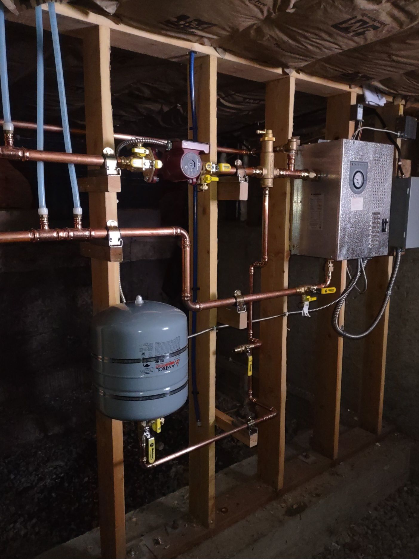 Copper plumbing and a gray water heater installed in an unfinished basement wall cavity.