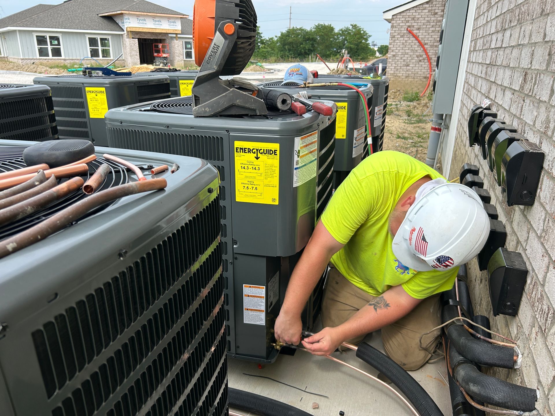 Construction worker connecting pipes to an air conditioning unit outside a building.