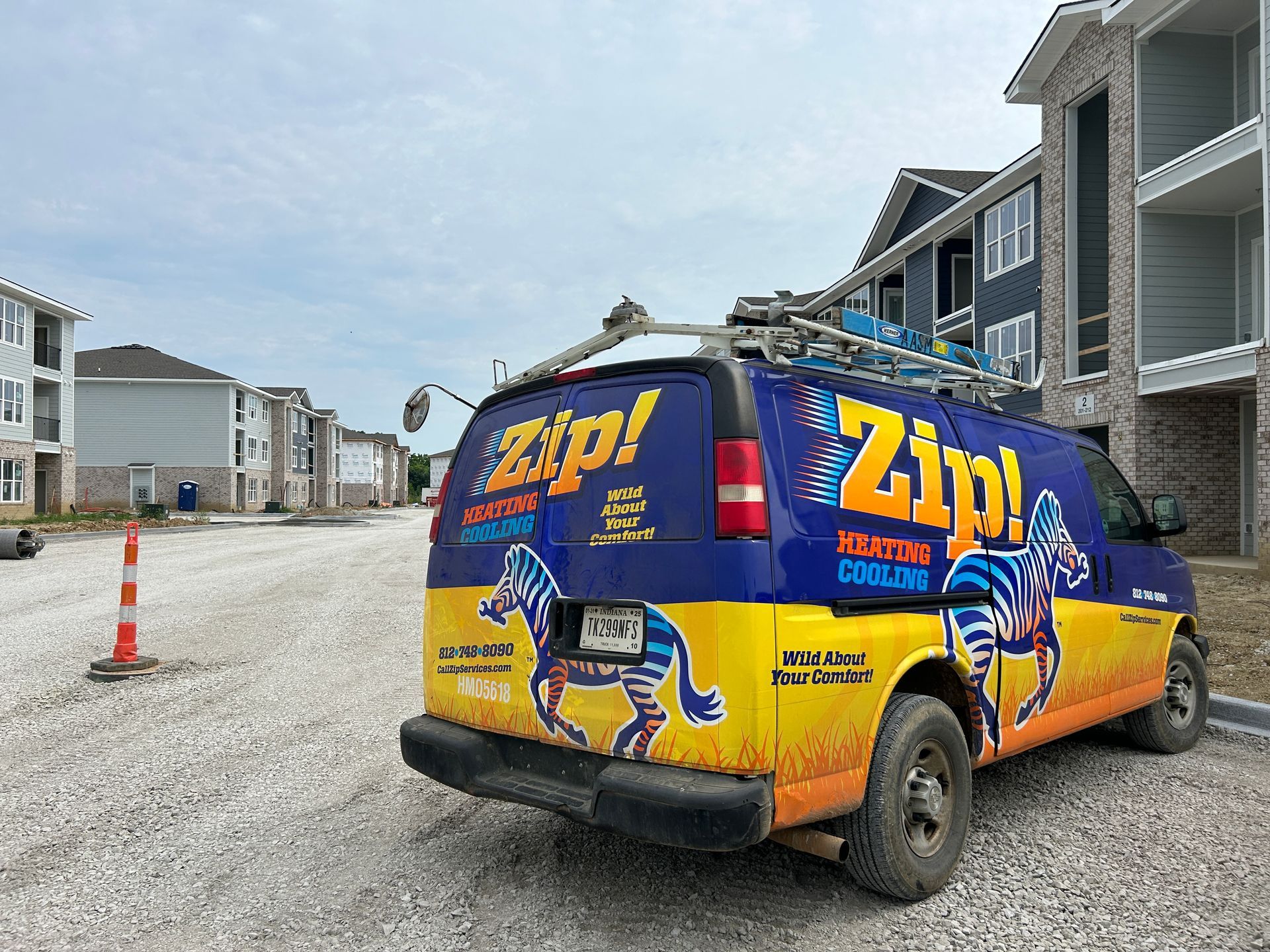 Zip! Roofing company van parked near apartment buildings on a gravel road under a cloudy sky.