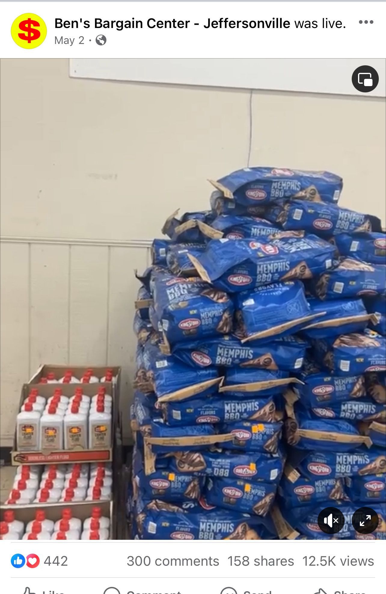 A large pile of blue bags, possibly pet food, next to cases of white and red bottles in a store.
