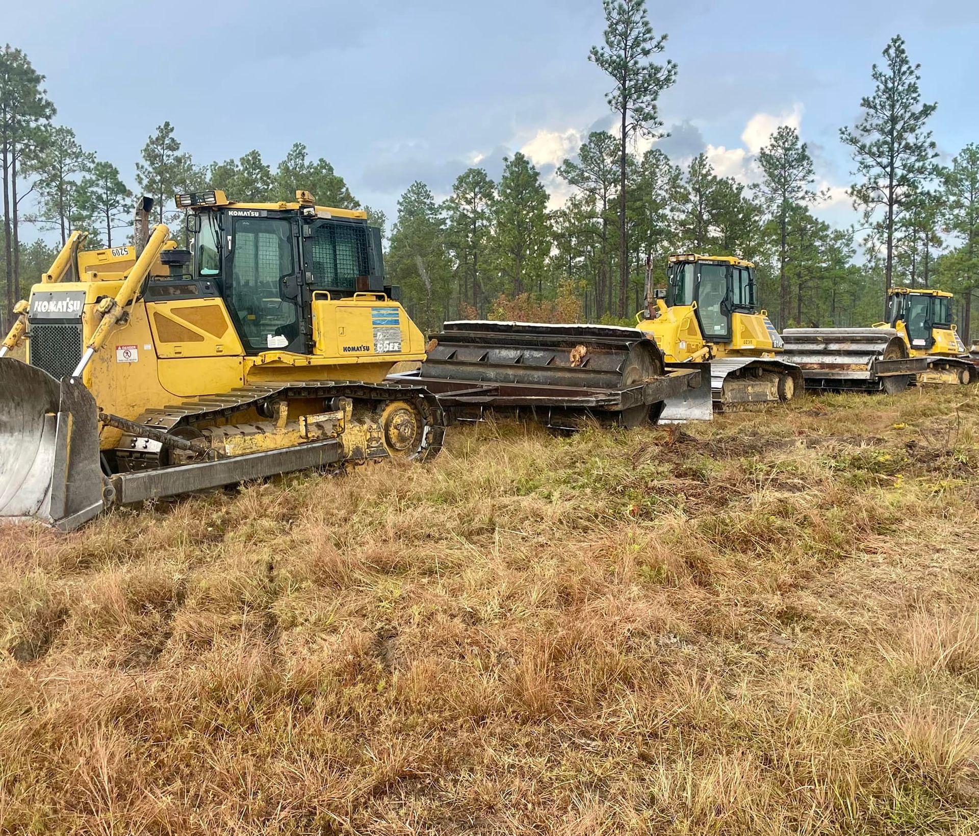 Yellow bulldozers pushing a cleared log on a grassy field under a cloudy sky