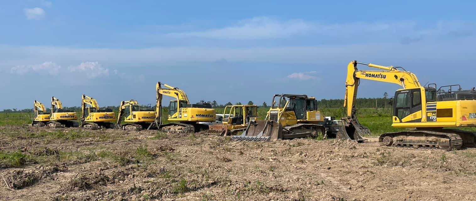 Yellow excavators lined up in a muddy field under a blue sky