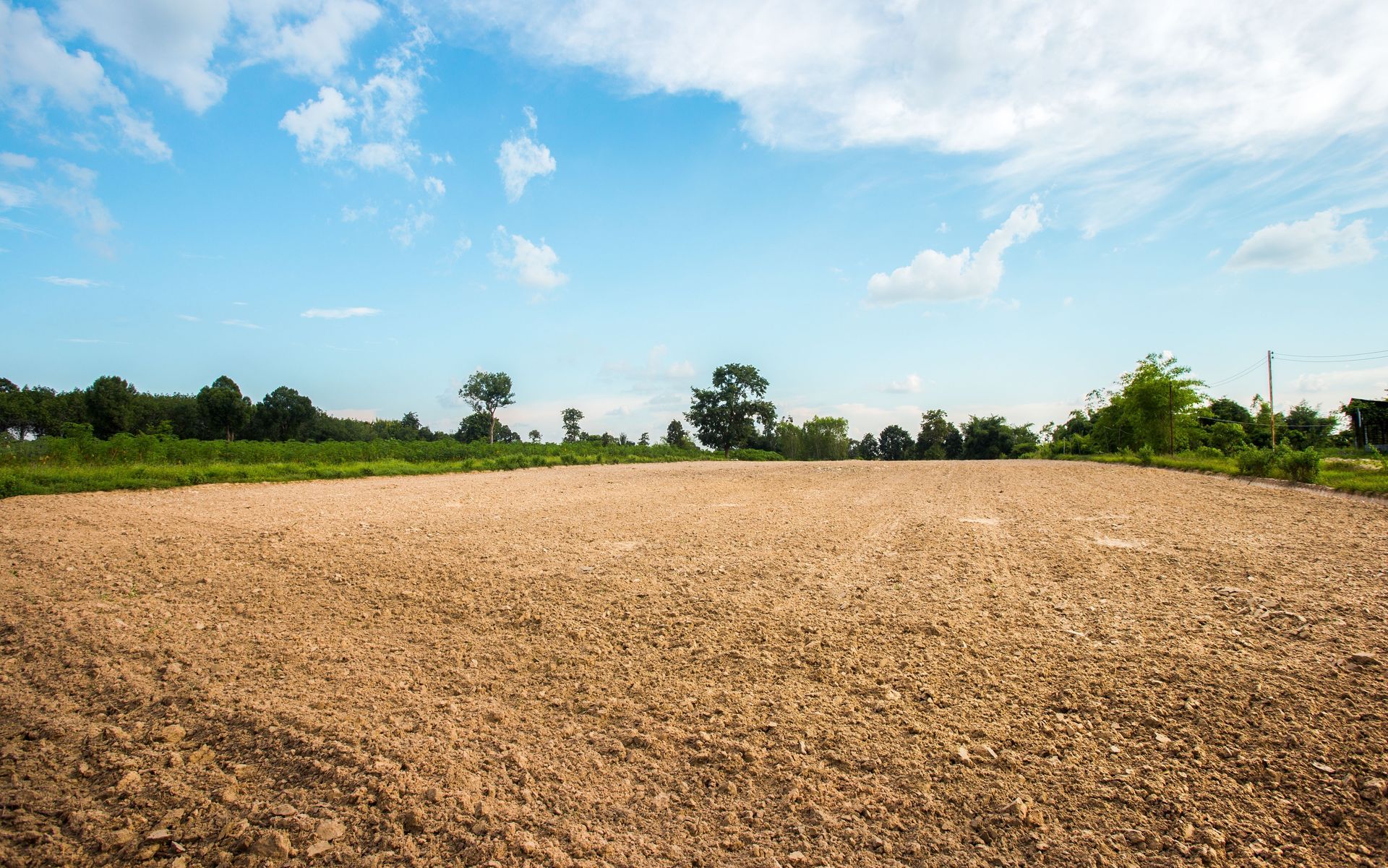 Plowed field under a bright blue sky with scattered clouds and a tree line in the distance