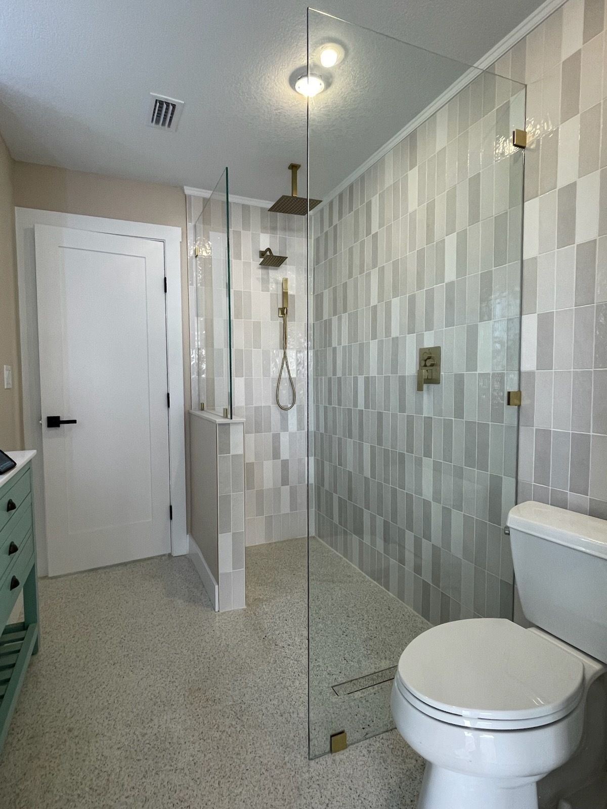 Modern bathroom with white toilet, tiled walls, glass shower, and vanity mirror adjoining a hall.