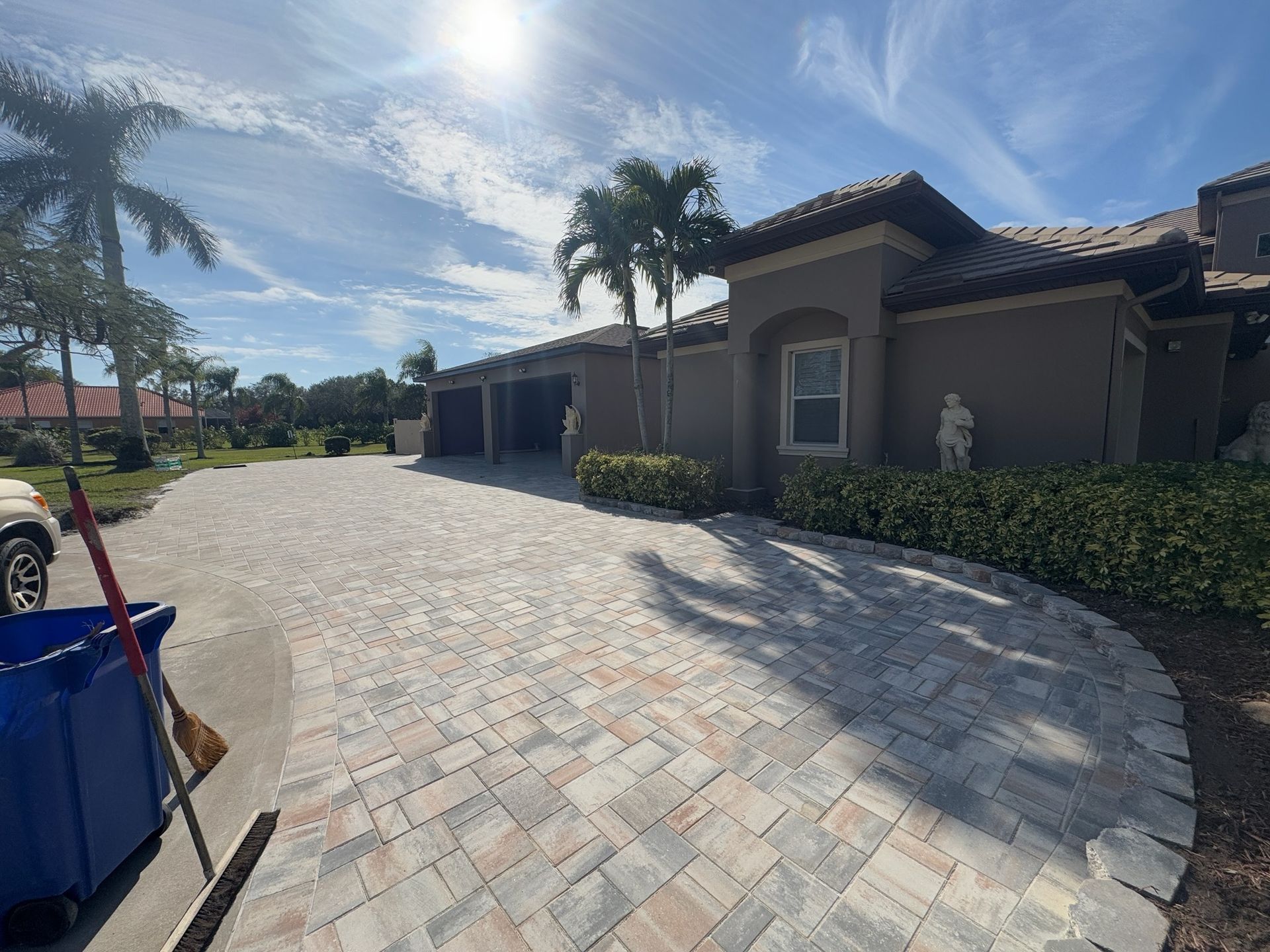 Curved stone driveway beside a stucco house with palm trees under a bright blue sky