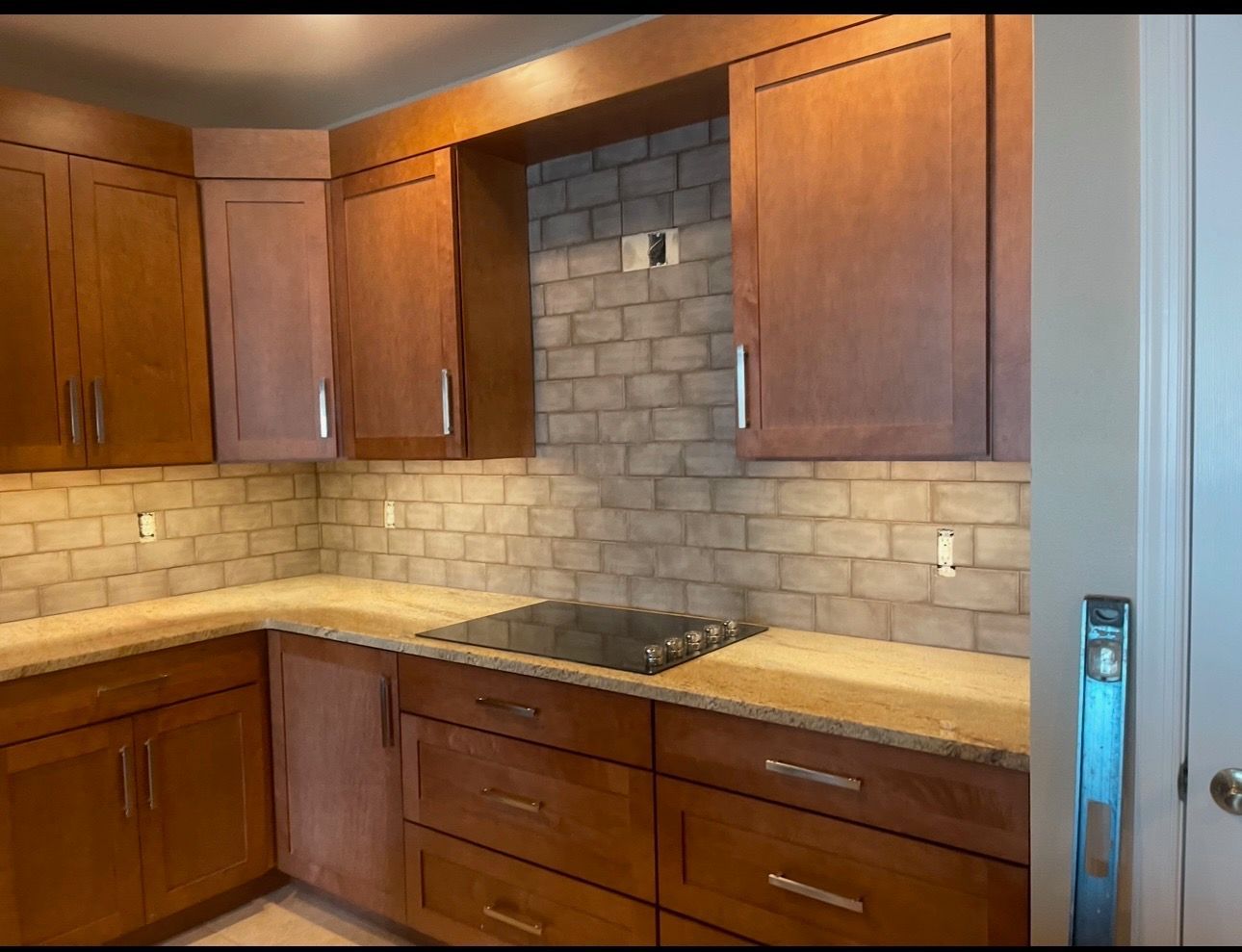 Modern kitchen with wood cabinets, beige tile backsplash, and a built-in cooktop on the counter.