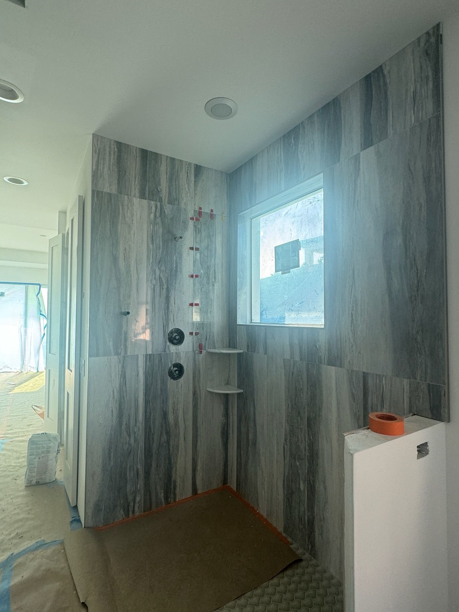 Bathroom shower area with blue-gray tiled walls, a window, and a small shelf.