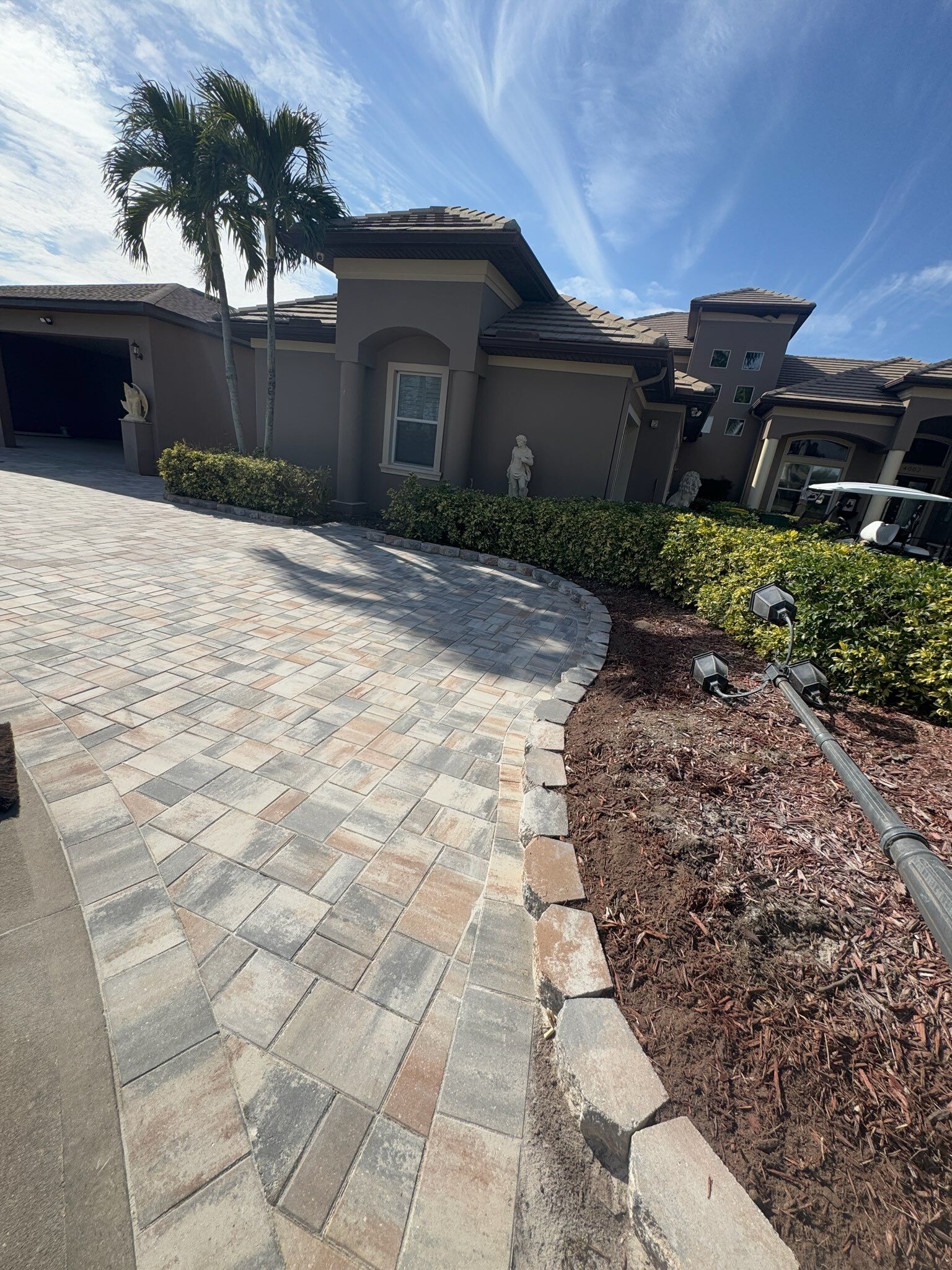 Sunlit driveway with paver stones leading to a stucco house and desert landscaping under a blue sky