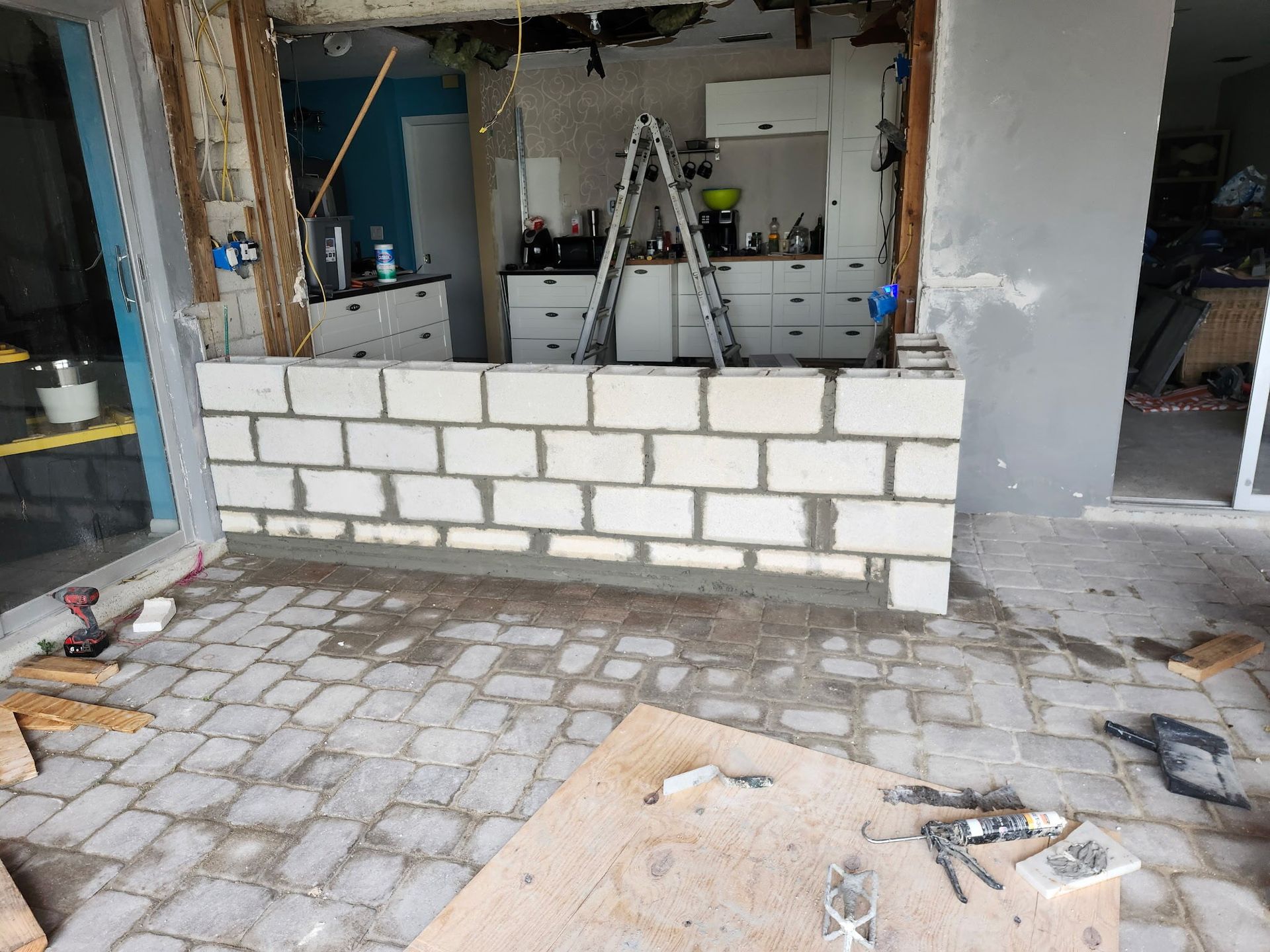 Partially built brick wall inside a room under renovation, with tools and ladders in the background.