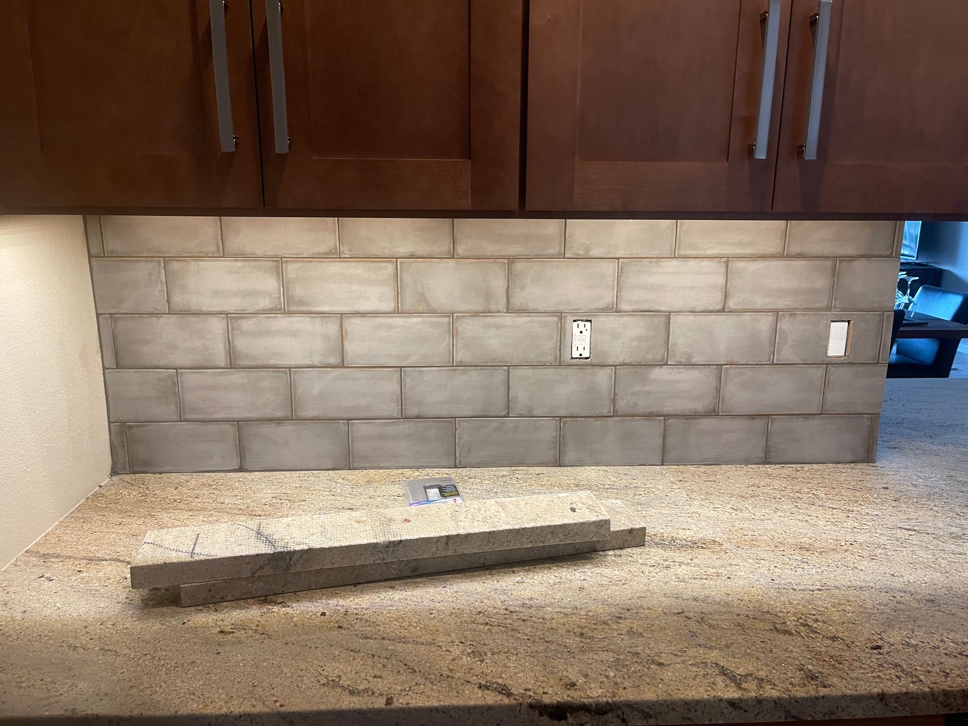 Kitchen countertop with stone tile backsplash, upper cabinets, and a long narrow object on the counter