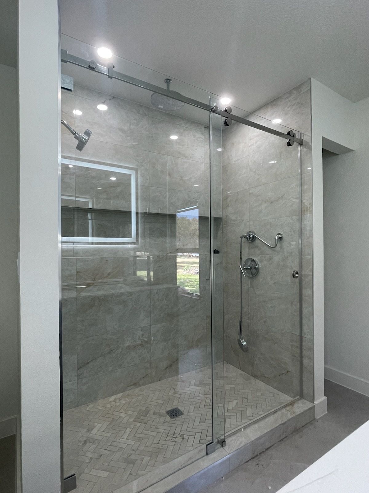 Modern glass walk-in shower with gray tile walls and chrome fixtures in a bright bathroom