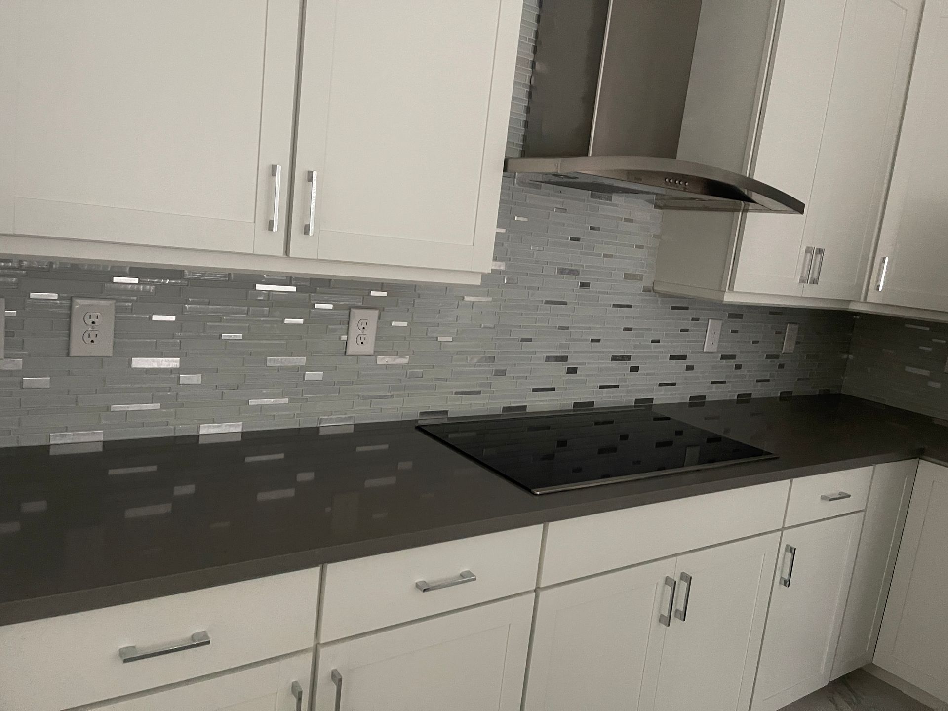 Modern kitchen with white cabinets, dark countertops, gray tile backsplash, and black cooktop.