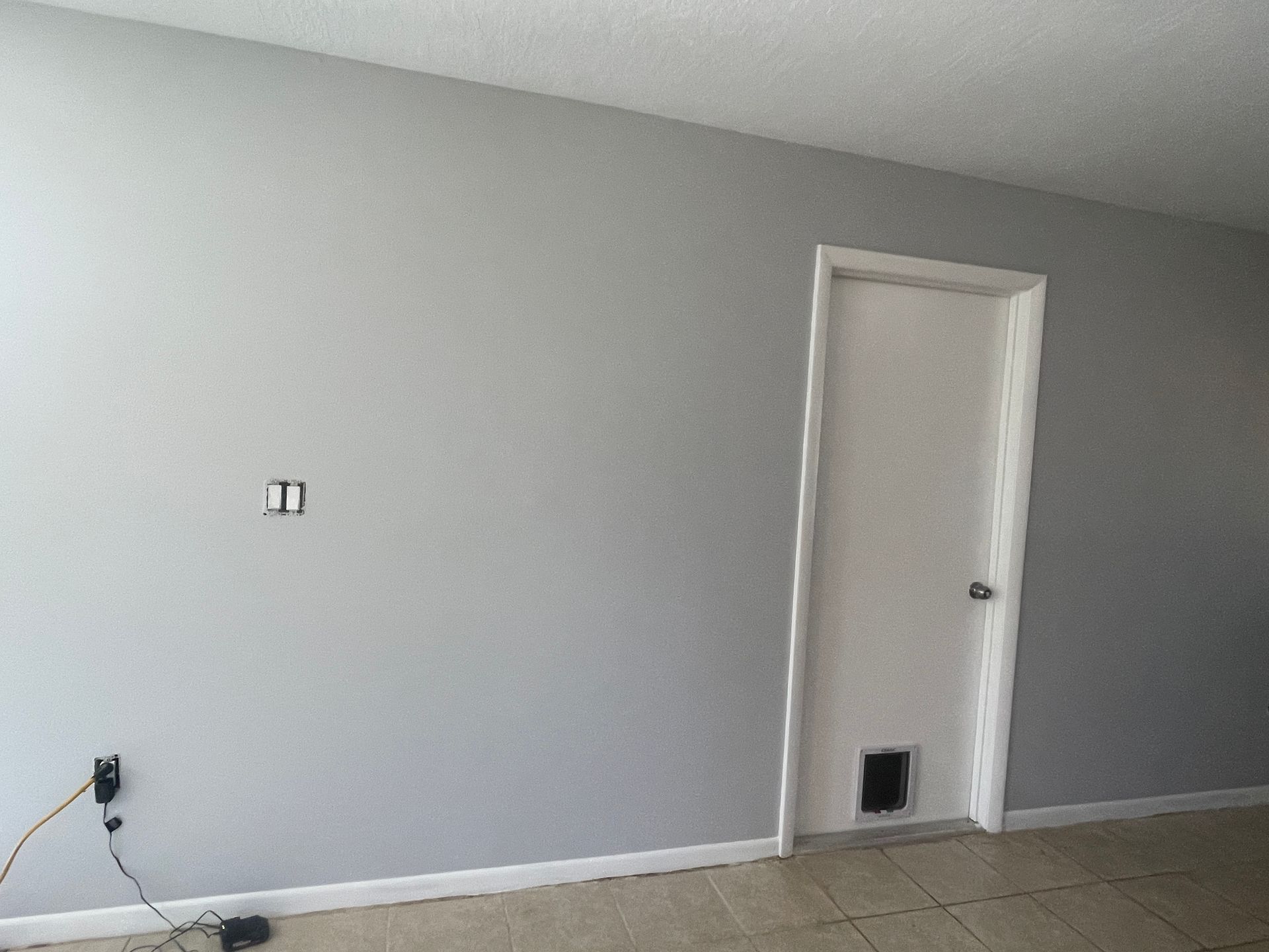 Empty gray room with white trim, a closed door, and visible wall outlets on the left.