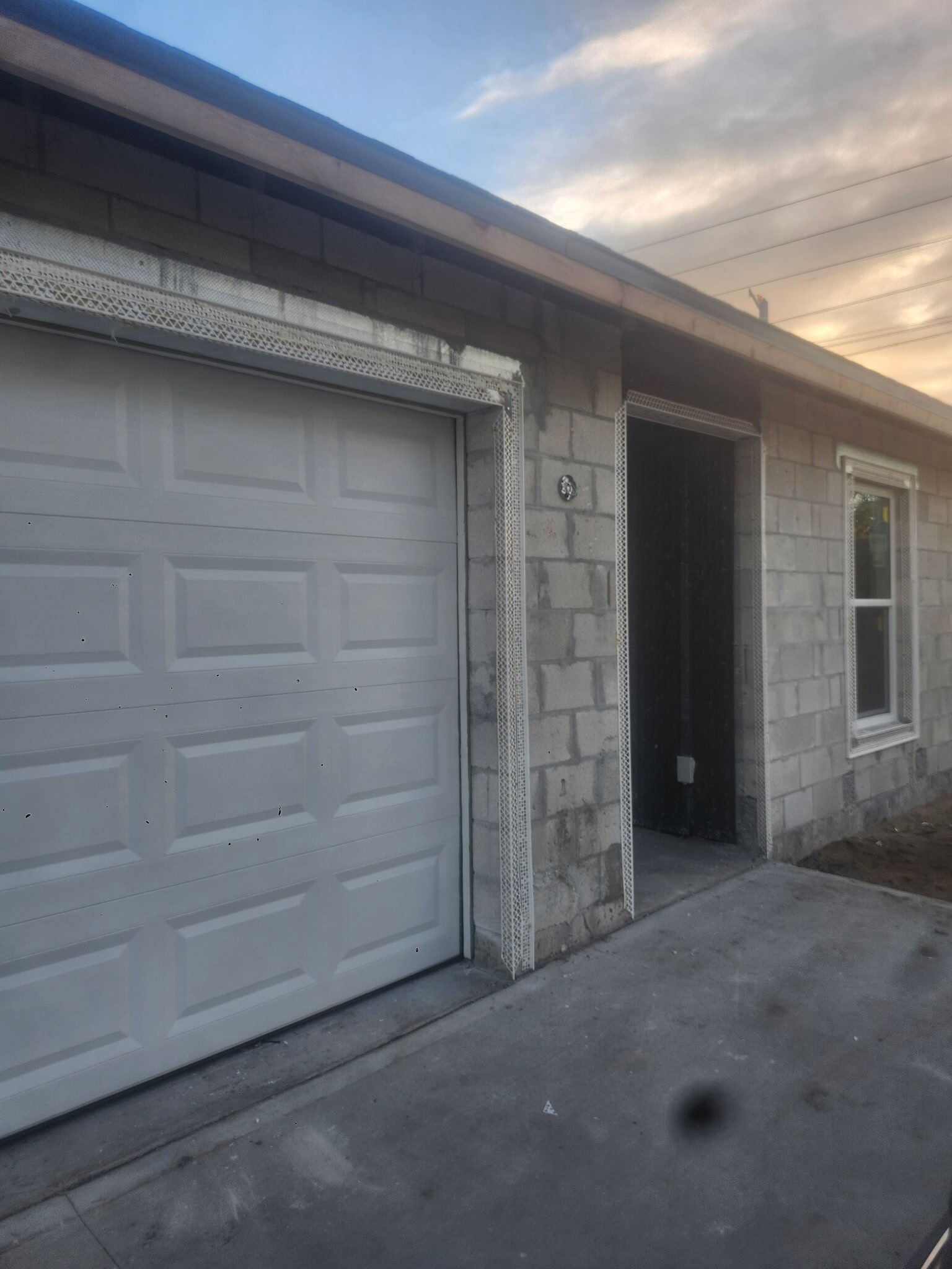 Single-story house exterior with a white garage door, front entryway, and concrete driveway at sunset