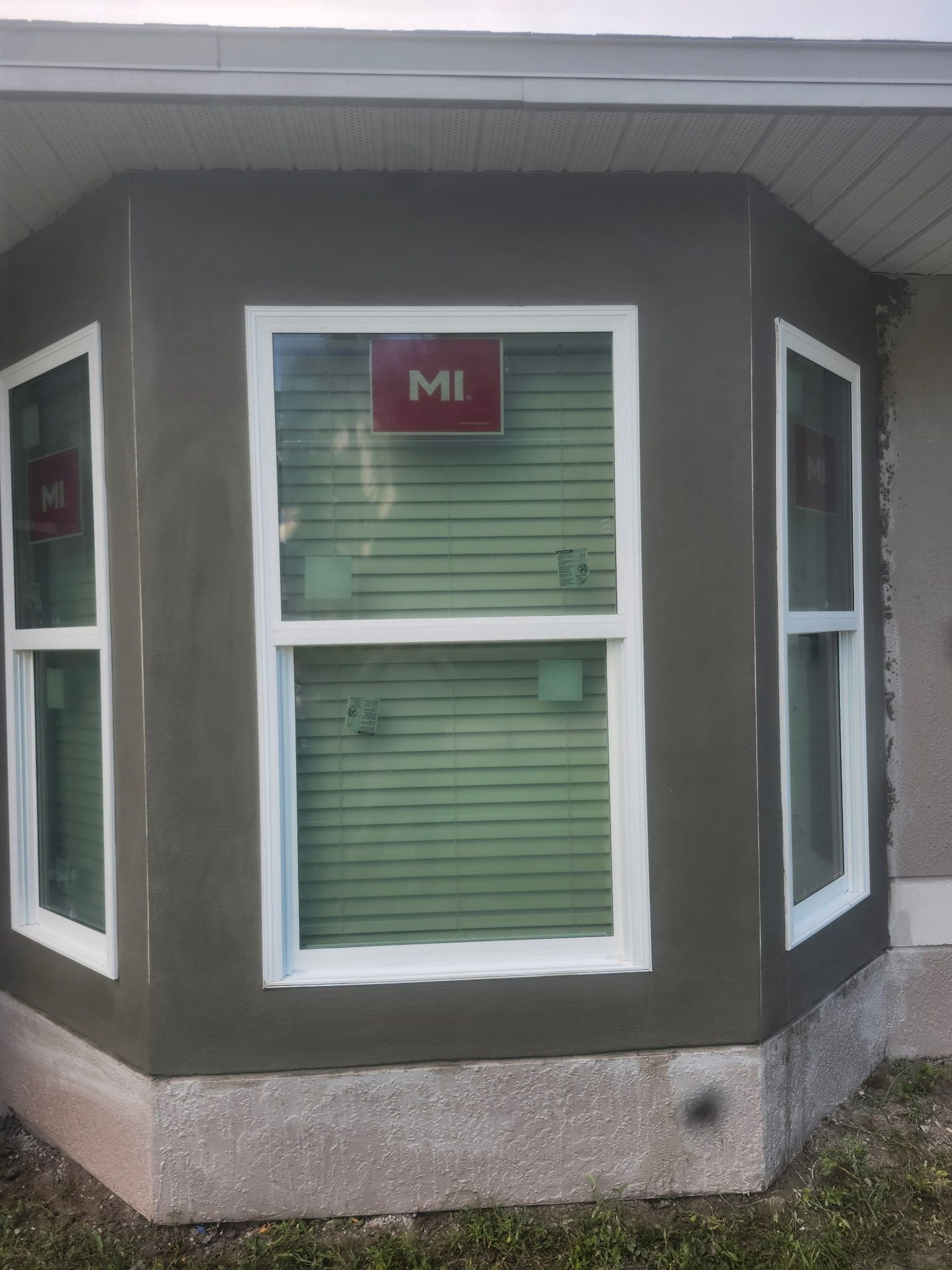 Bay window with green blinds and white trim on a gray house exterior