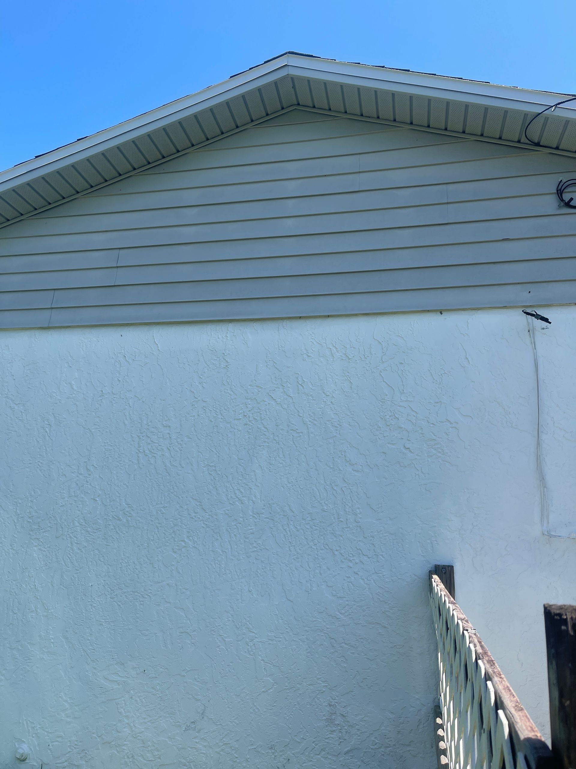White house exterior with gray siding under a blue sky, seen from below.